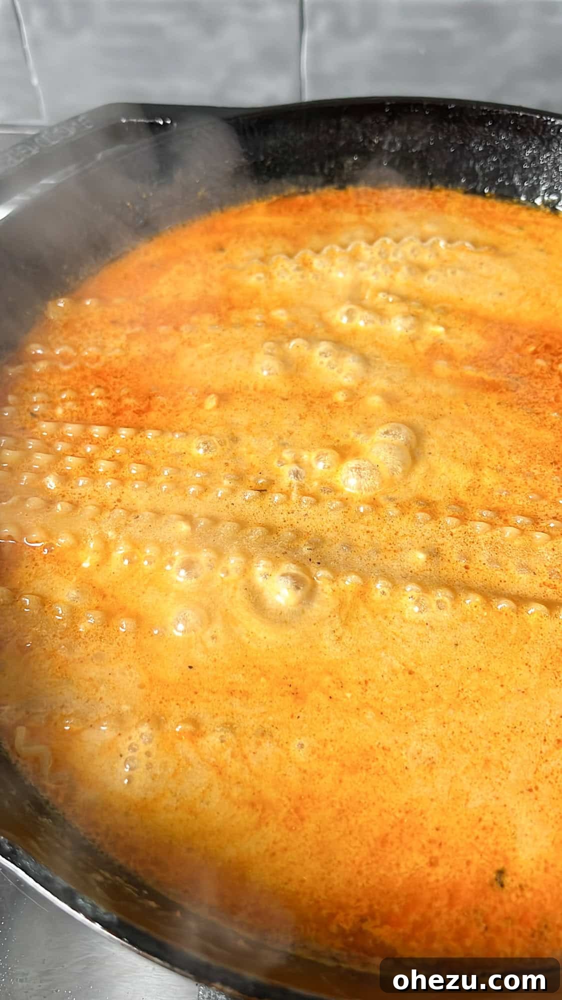 Dry fettuccine pasta being gently submerged into the simmering buffalo alfredo sauce in a skillet