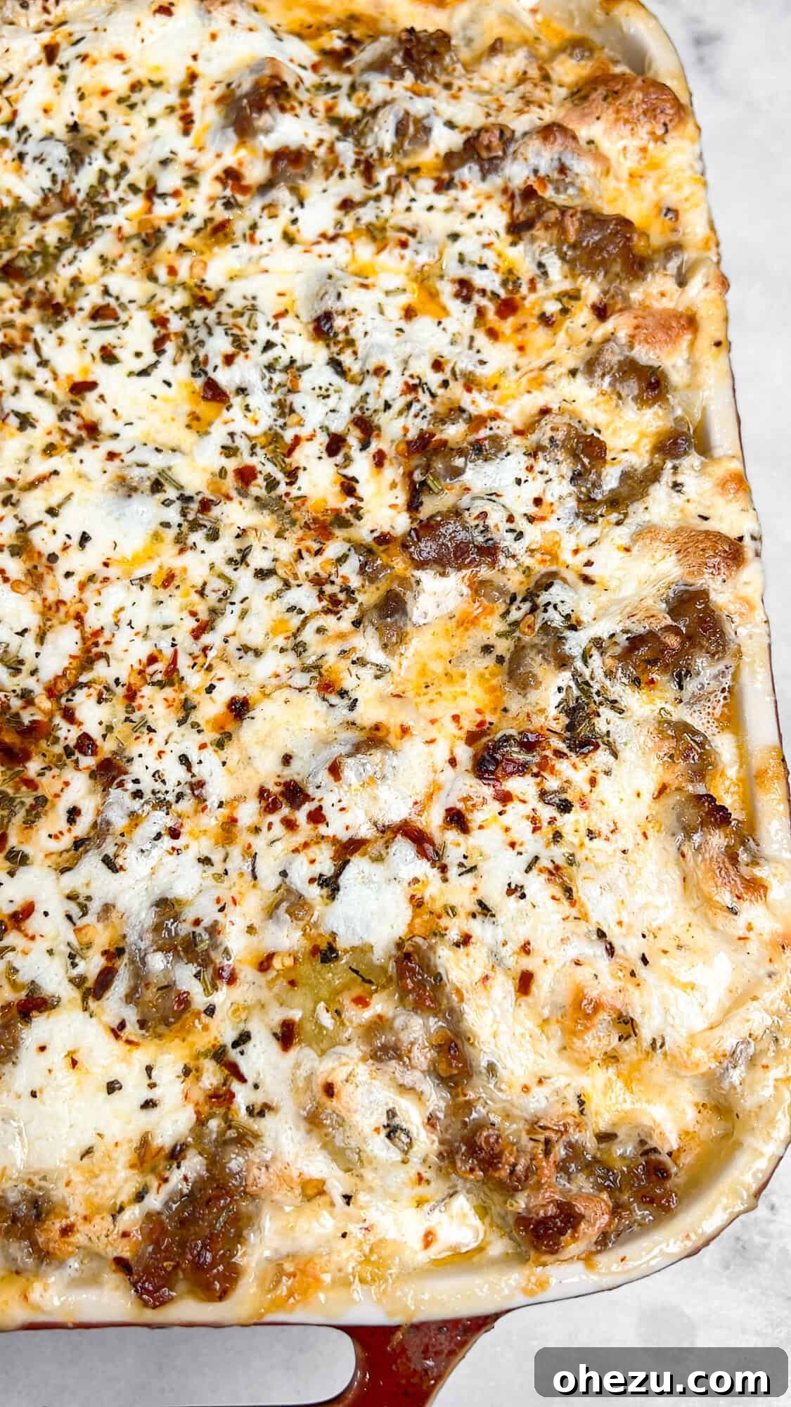 A serving of Alfredo Ravioli Lasagna with visible layers of pasta, sausage, and cheese on a plate.