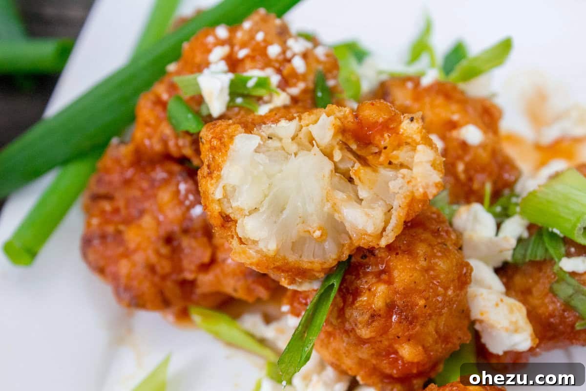 Platter of freshly made Buffalo Cauliflower Bites, elegantly garnished with crumbled blue cheese and finely chopped green onions.