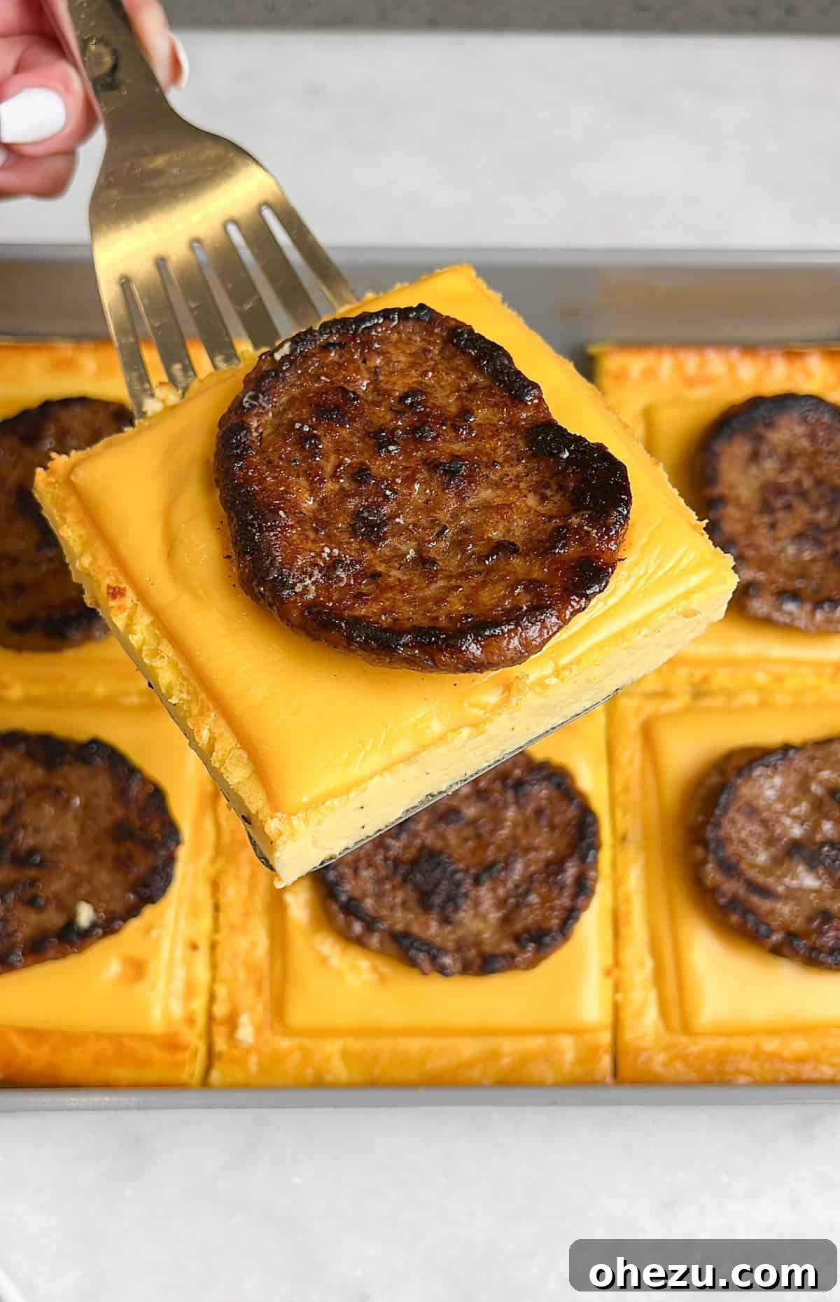One-Pan Protein Power Breakfast Sandwiches 4 Overhead view of a cooked sheet pan egg layer with melted cheddar cheese and cooked sausage patties, ready to be sliced for assembly