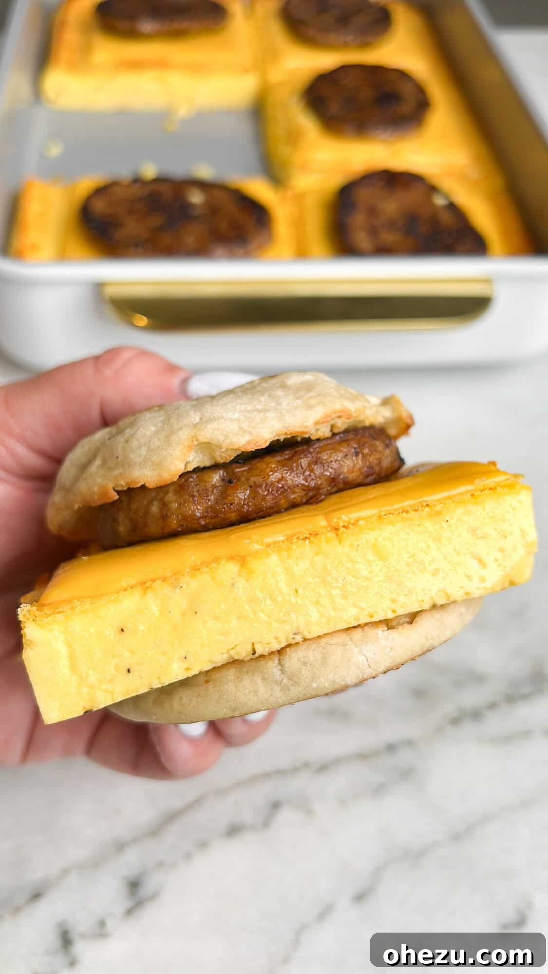 One-Pan Protein Power Breakfast Sandwiches 5 Ingredients laid out for high protein sheet pan breakfast sandwiches, including eggs, cottage cheese, cheese, hot sauce, cornstarch, sausage, and English muffins