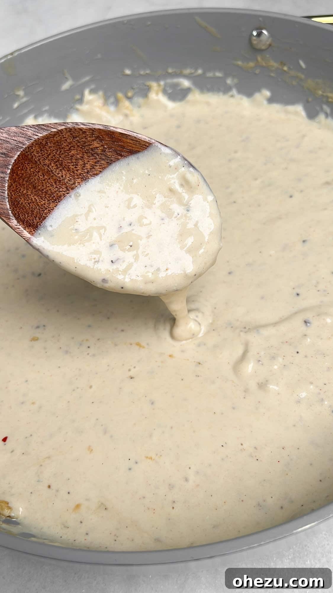 Close-up shot of creamy alfredo sauce being tossed with cooked angel hair pasta