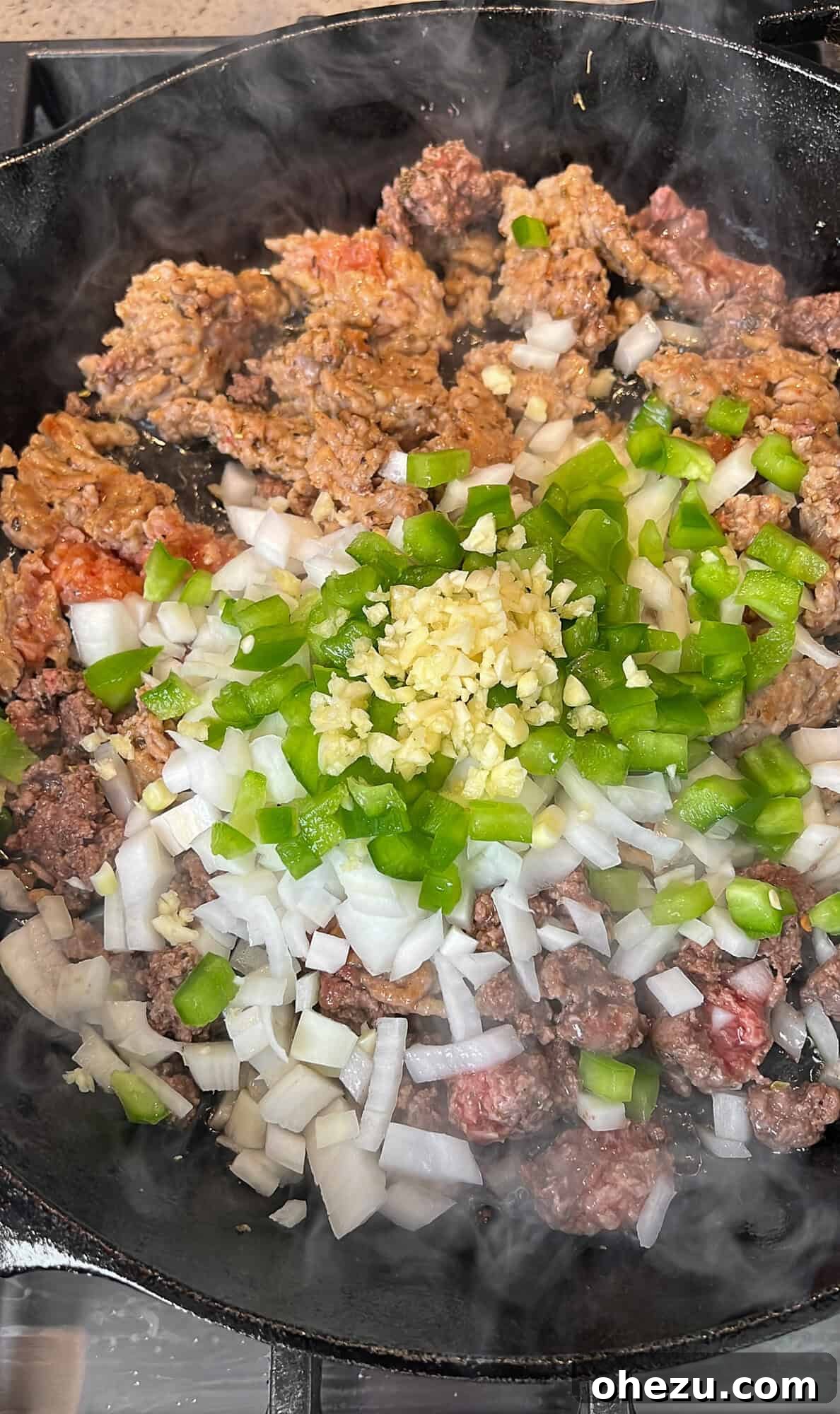 Sautéing ground beef, Italian sausage, and vegetables in a skillet for the marinara meat sauce