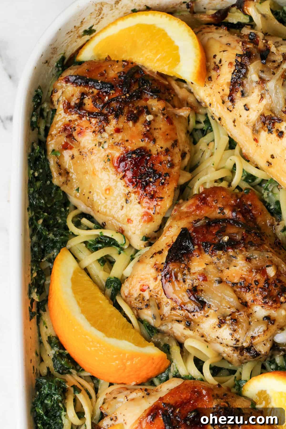 Golden brown baked chicken over linguini with fresh orange wedges and herbs