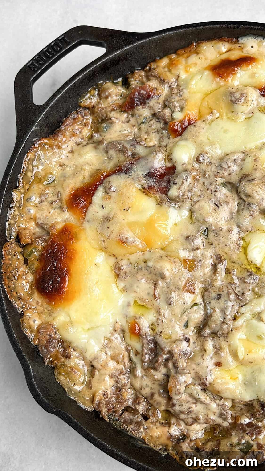 Golden brown Philly Cheesesteak Dip in a cast iron skillet, bubbling and ready to serve