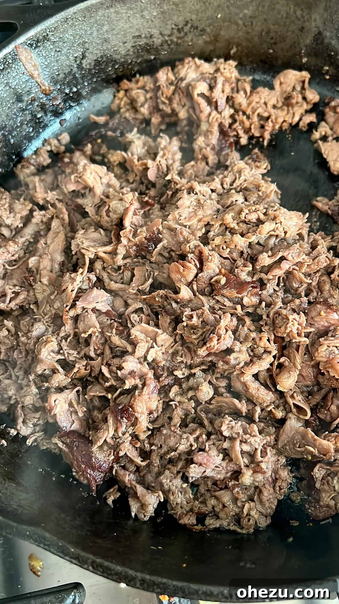Shaved ribeye steak cooking in a skillet, chopped into small pieces