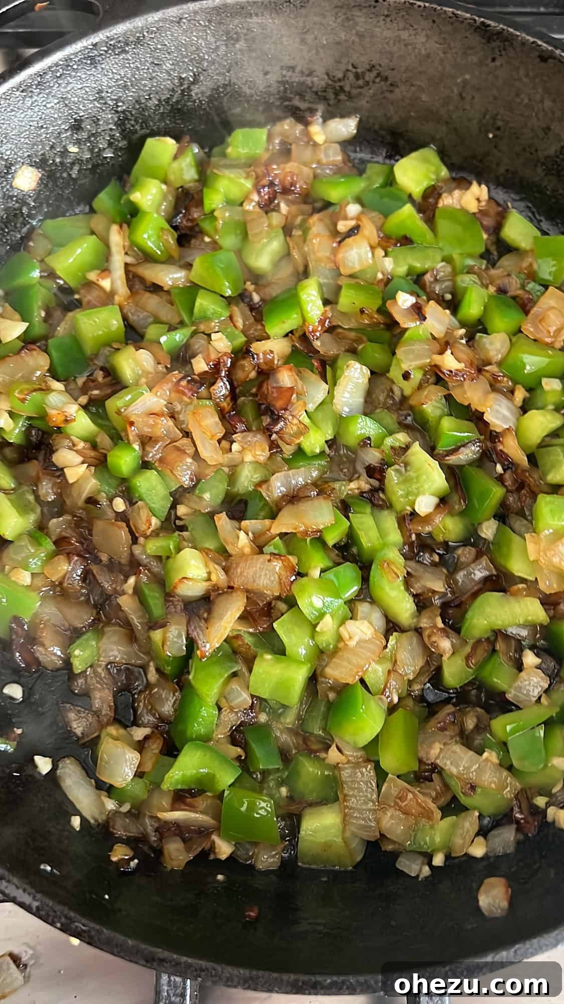 Caramelizing onions and green bell peppers in a skillet, releasing their sweet aromas