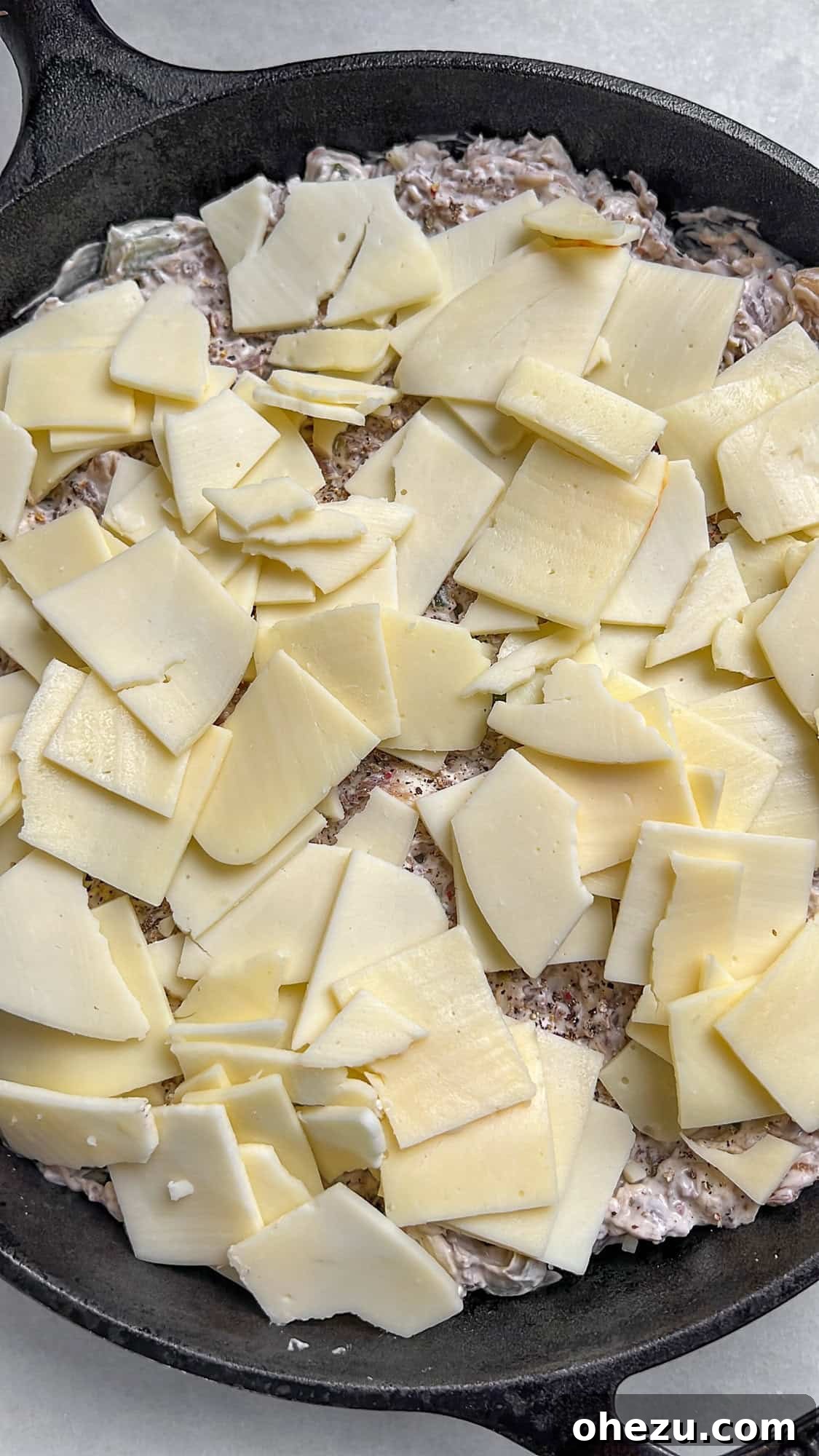 Unbaked Philly Cheesesteak Dip in a baking dish, topped with cheese, ready for the oven