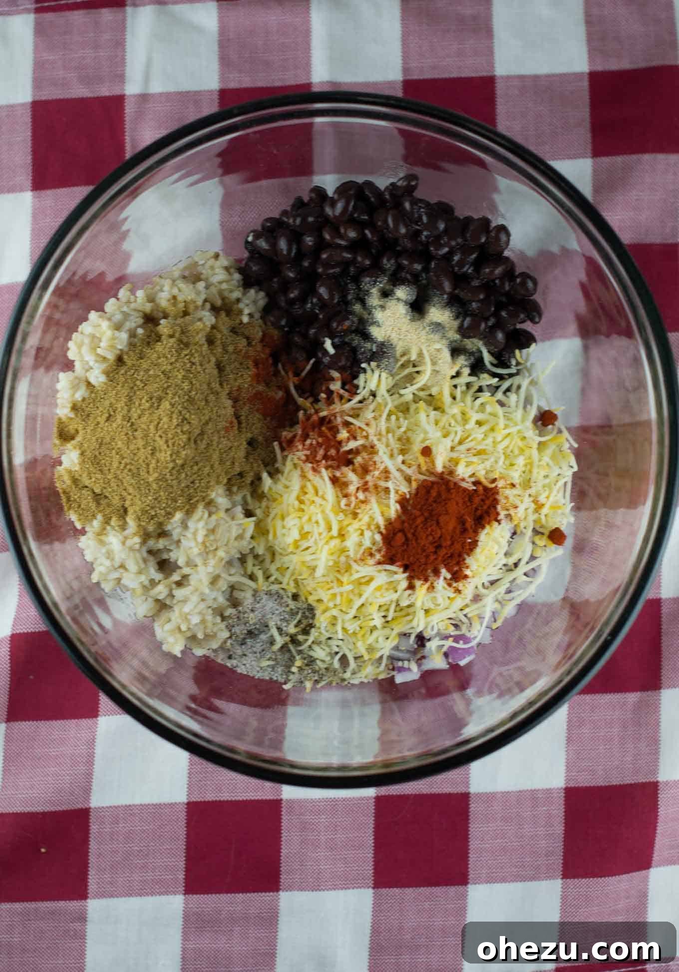 No-Fuss Slow Cooker Plant-Based Stuffed Peppers 6 Adding black beans, Mexican cheese, and diced red onion to brown rice in a mixing bowl.