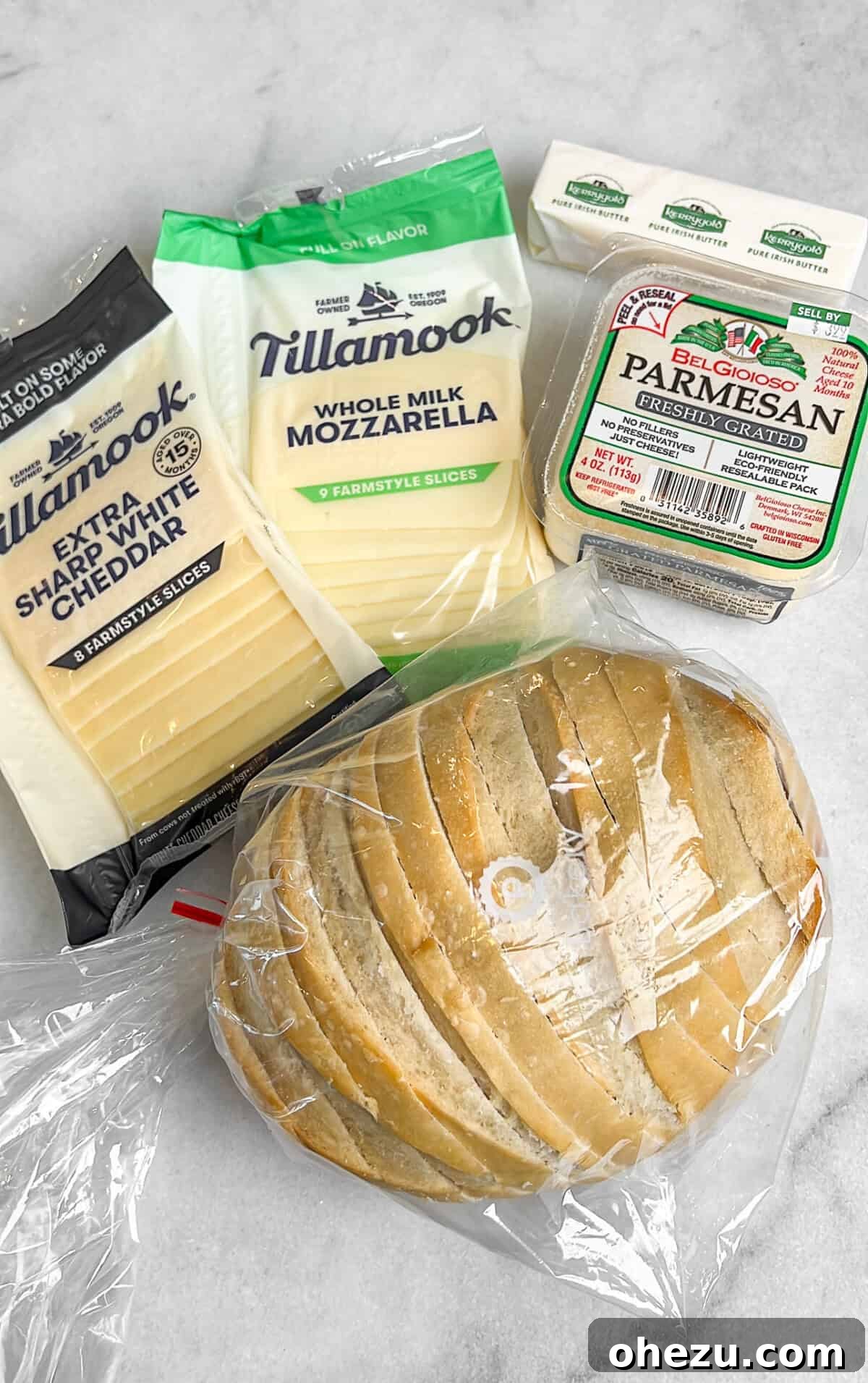 Individual ingredients for the copycat Starbucks grilled cheese spread out on a wooden board, including sourdough bread, butter, parmesan, garlic, sharp white cheddar, and mozzarella cheese.