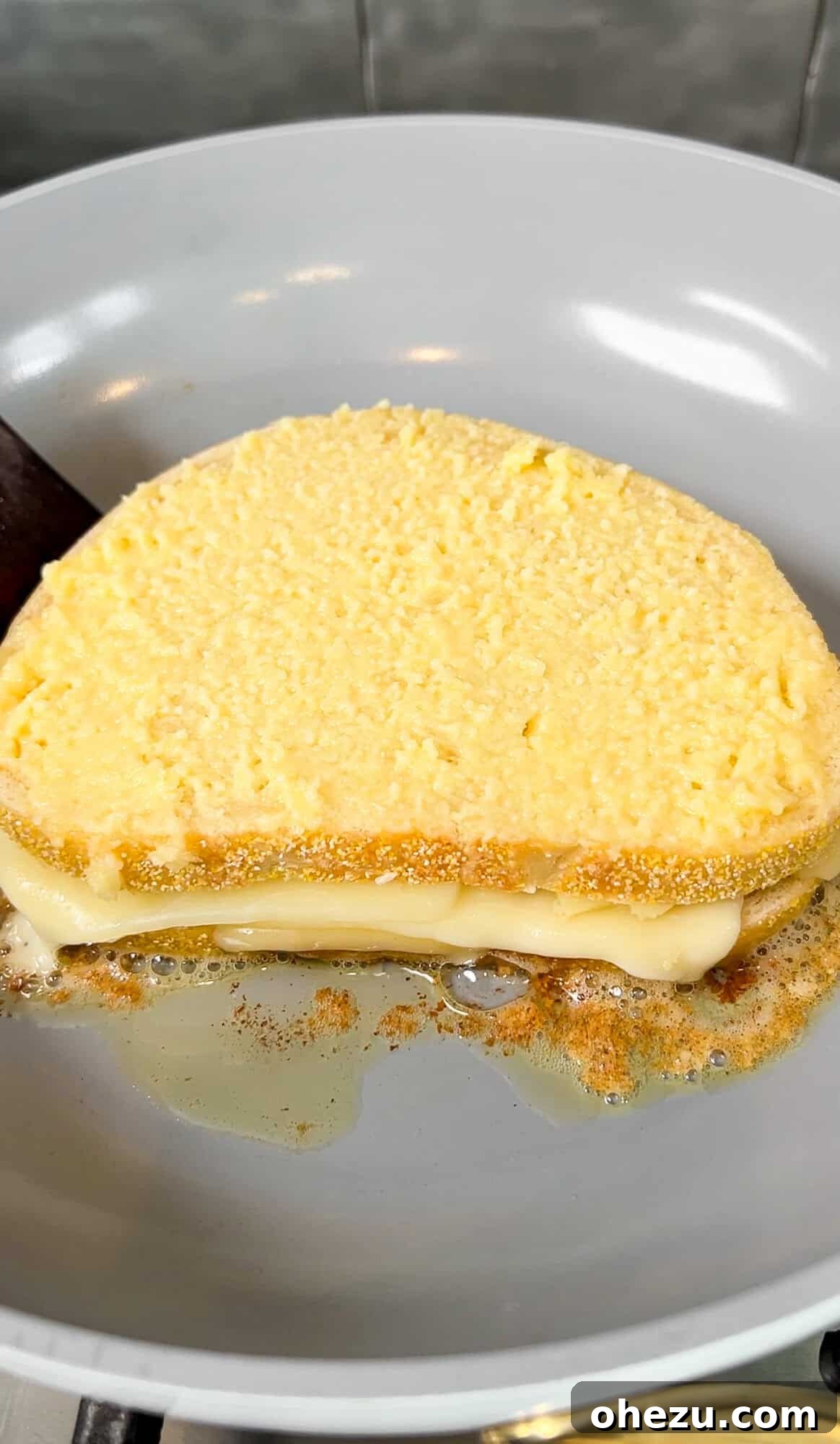 A copycat Starbucks grilled cheese sandwich cooking in a nonstick skillet, turning golden brown.