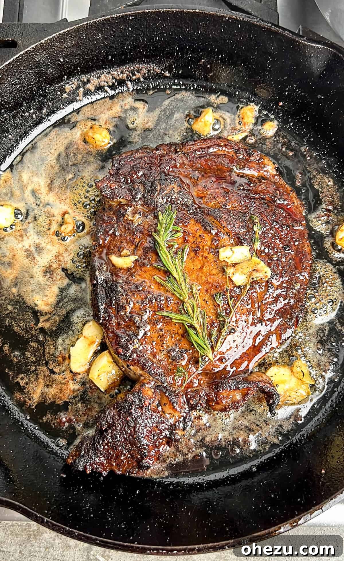 Cognac Kissed Cast Iron Steak 9 A cast iron steak sizzling with butter and herbs in the pan.