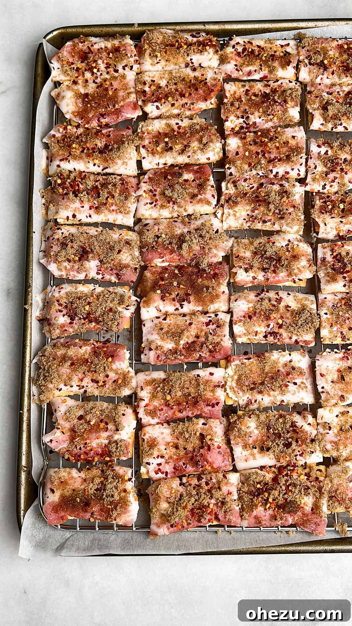 Assembled Boursin Candied Bacon Crackers on a baking rack, topped with cheese, bacon, brown sugar, and red pepper flakes, ready for the oven.