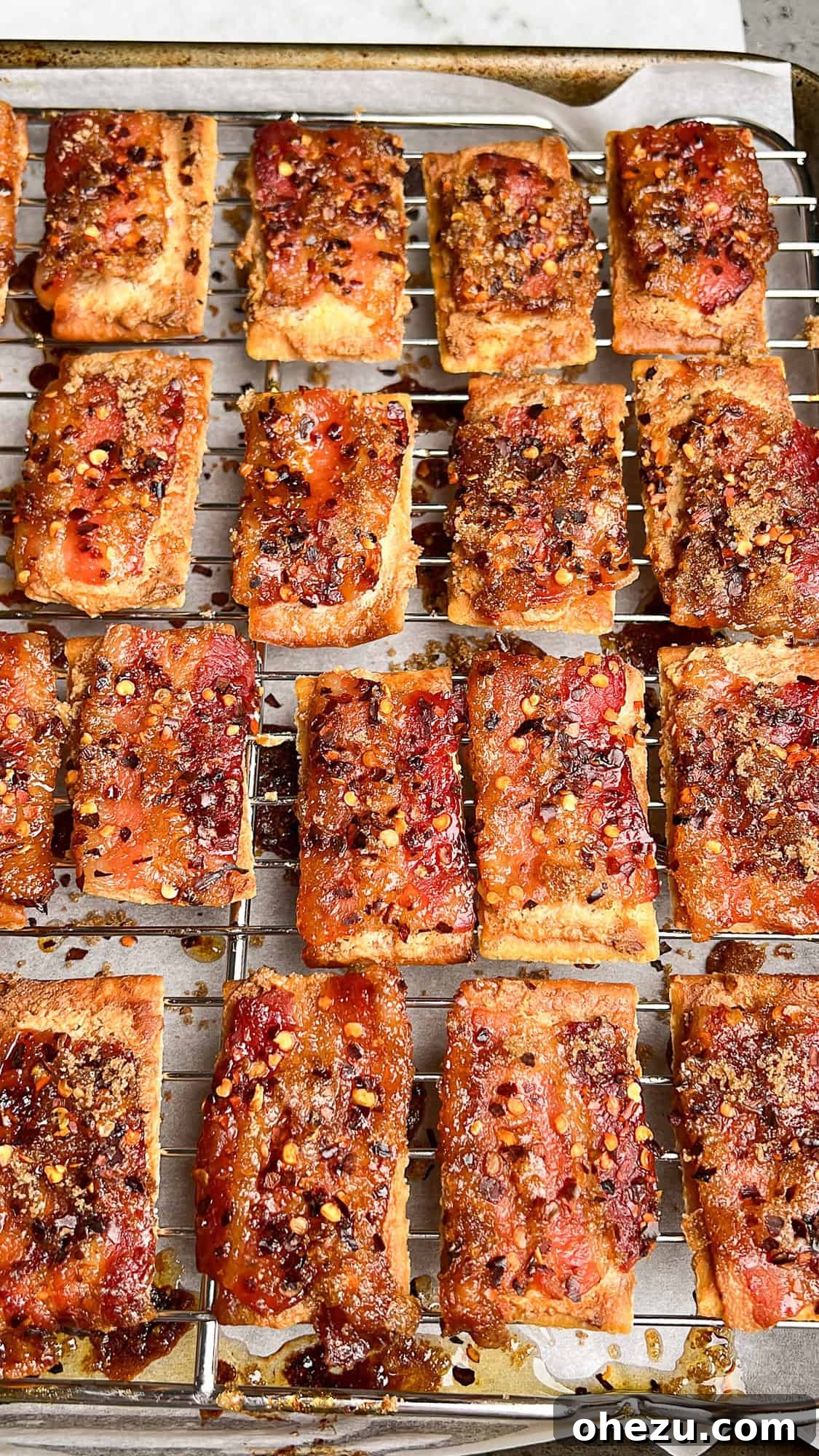 Boursin Candied Bacon Crackers baking in the oven on a wire rack, the bacon sizzling and caramelizing.