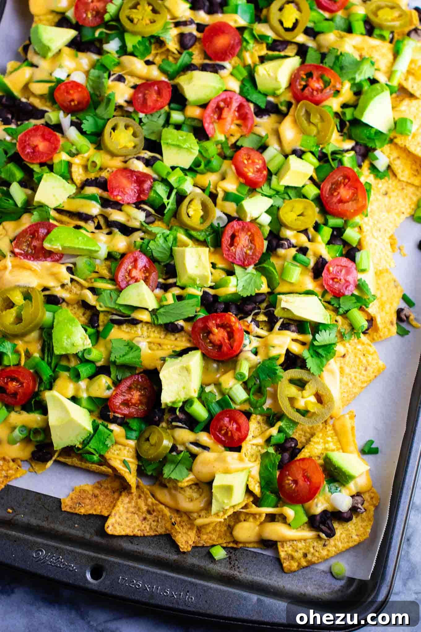 Ultimate Loaded Vegetable Nachos 3 Close-up shot of loaded veggie nachos showcasing the crunchy chips, black beans, green peppers, and creamy nacho cheese sauce. #veggienachos #vegetarian #nachocheese #nachocheesesauce