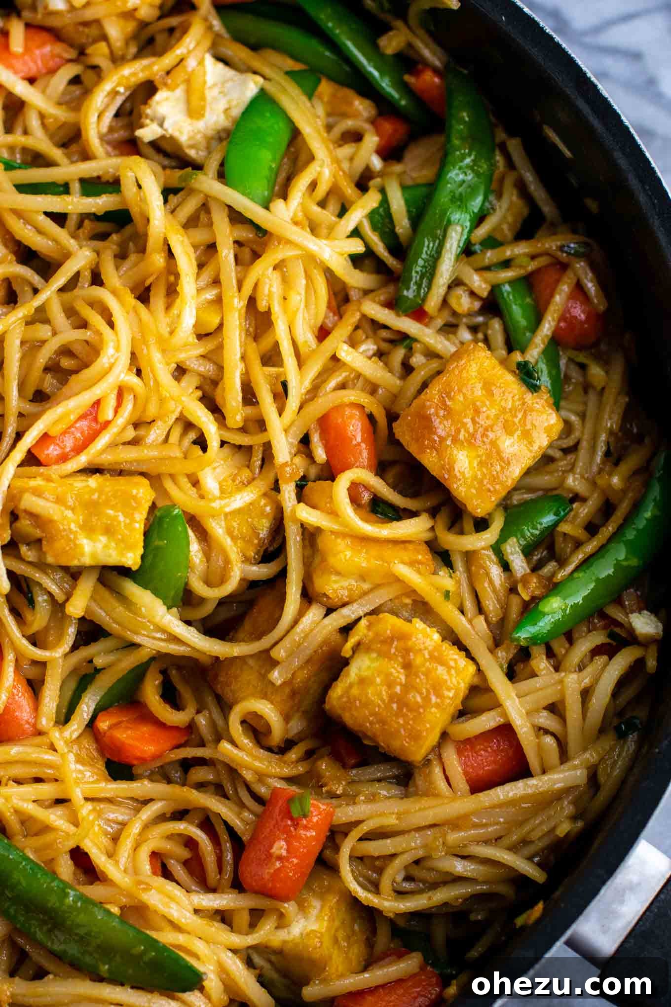 Close-up of vibrant tofu stir fry noodles featuring crisp sugar snap peas and carrots, coated in a savory sauce.