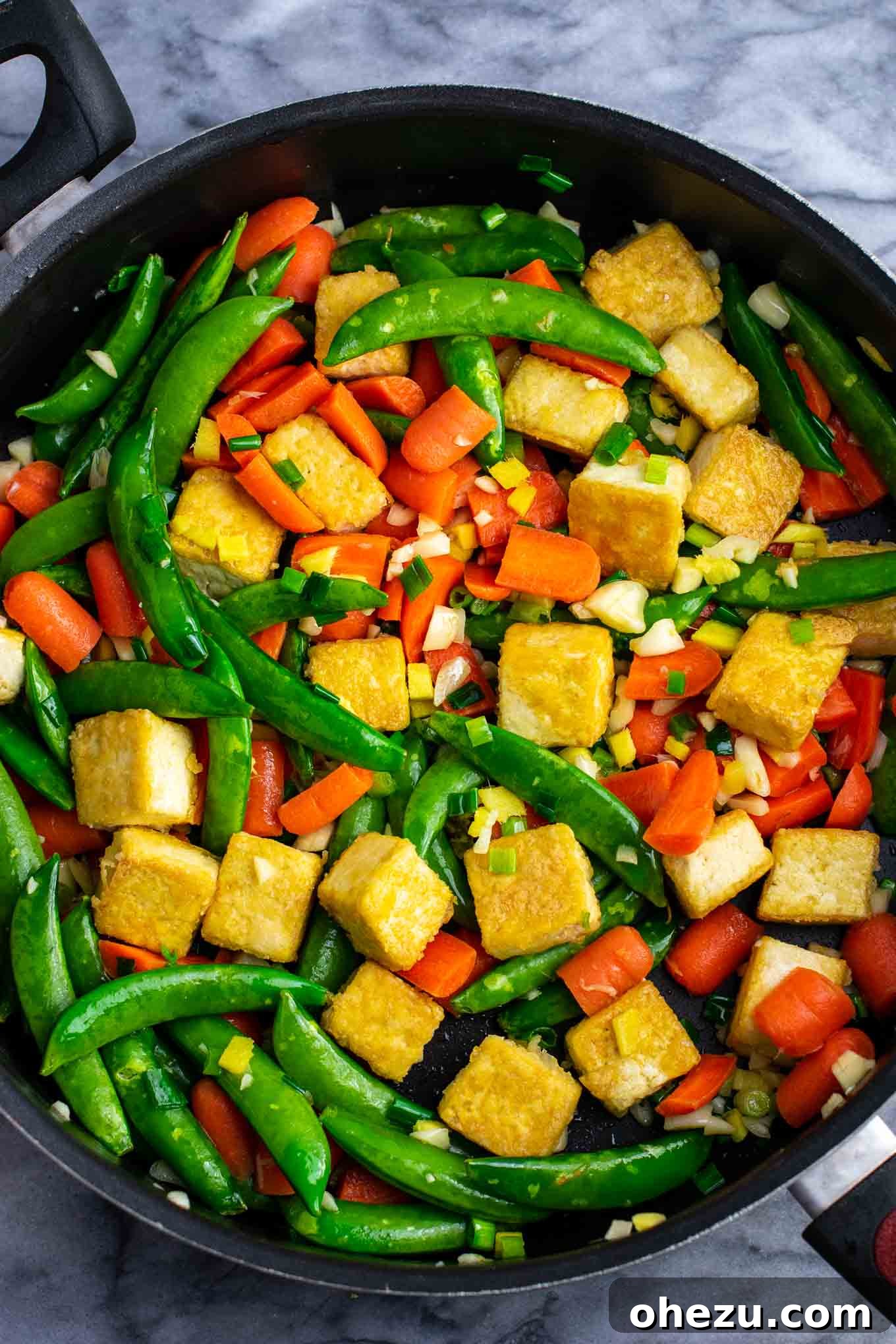 Freshly cooked rice noodles being added to the colorful tofu and vegetable stir fry.