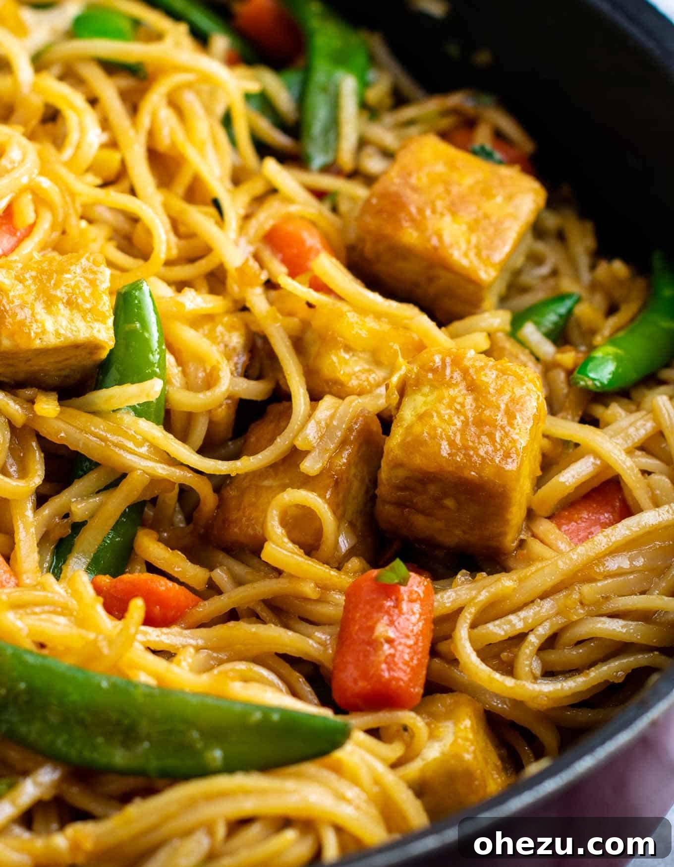 Finished vegan stir fry noodles with crispy tofu, sugar snap peas, and carrots, glistening with homemade sauce.