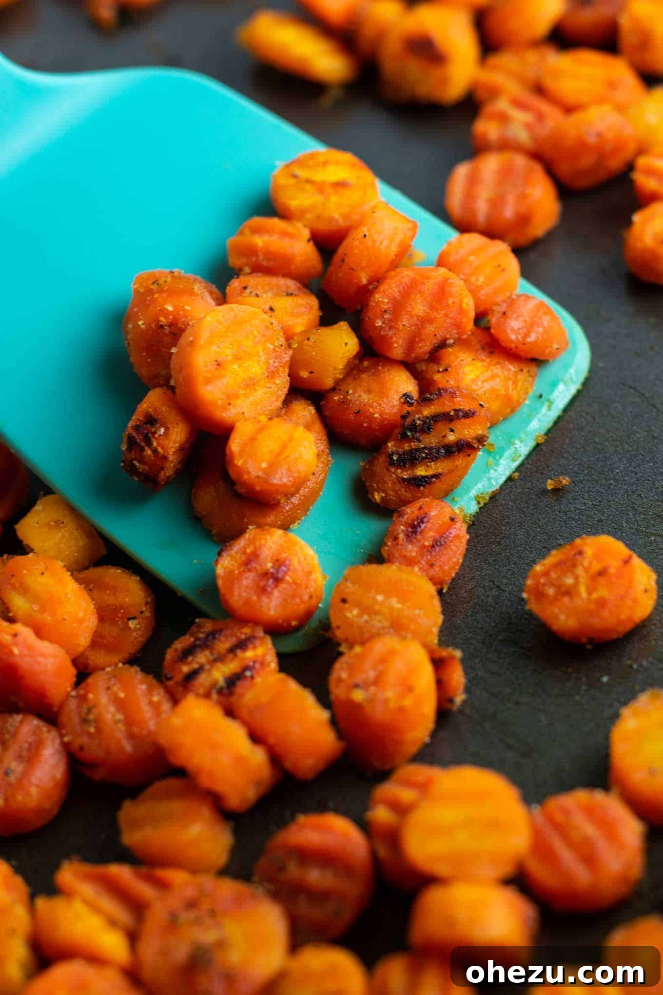 A blue spatula scooping a generous serving of finished roasted frozen crinkle-cut carrots, highlighting their succulent appearance.