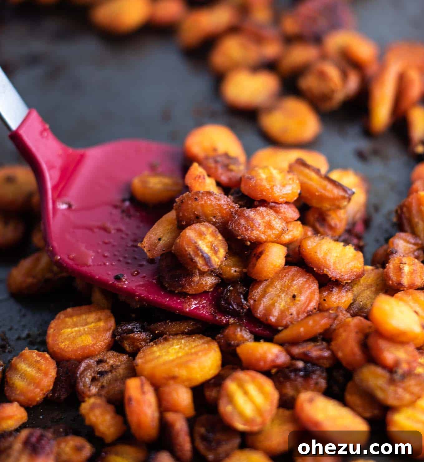 A red spatula with a heap of roasted carrots, showing their tender interior and inviting aroma.