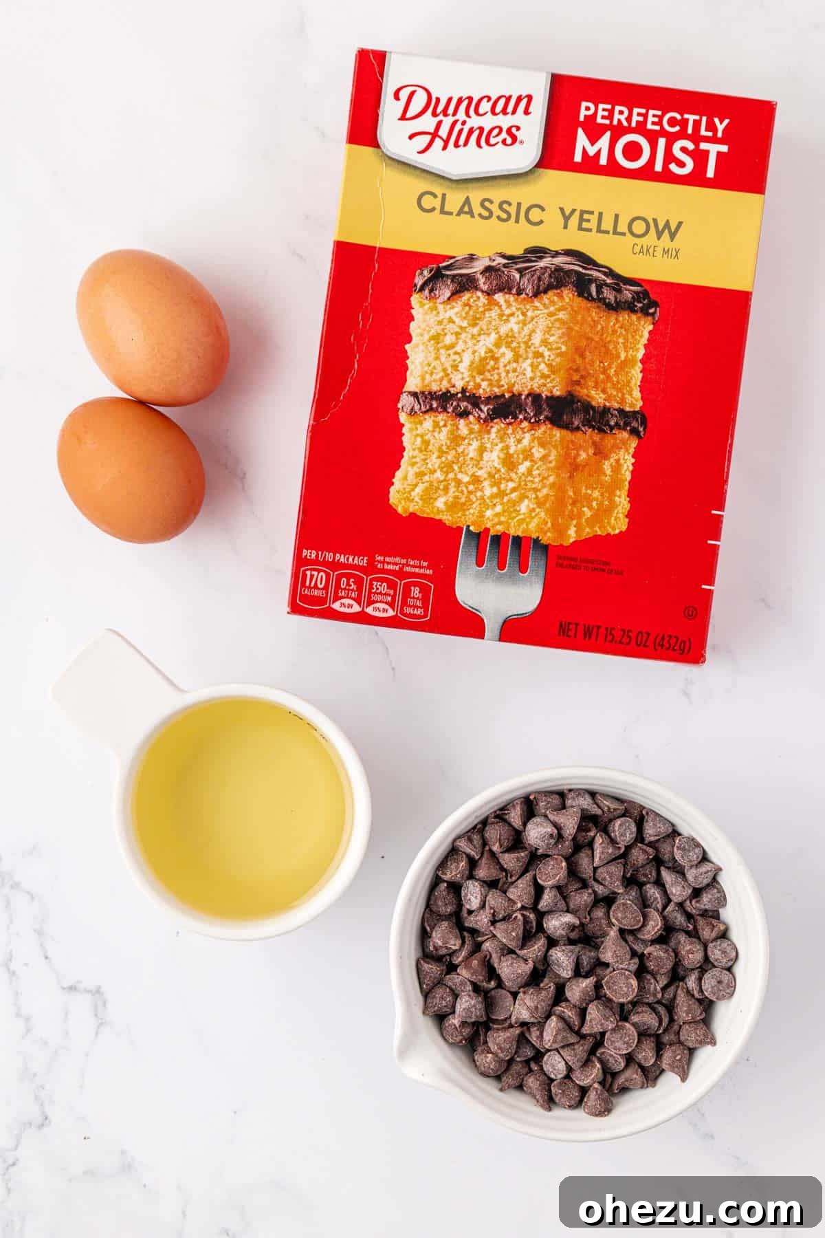 Ingredients laid out: a box of yellow cake mix, two eggs, a bottle of olive oil, and a bowl of chocolate chips