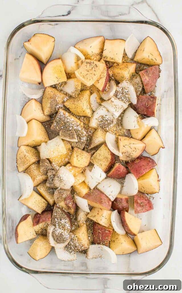 Red potatoes, onions, oil, and spices mixed in a glass baking dish