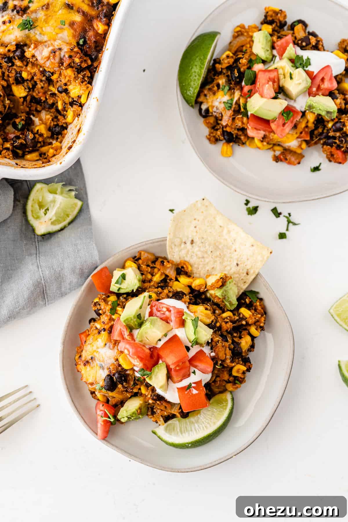 quinoa enchilada casserole on a white plate topped with sour cream, tomato, avocado, and lime