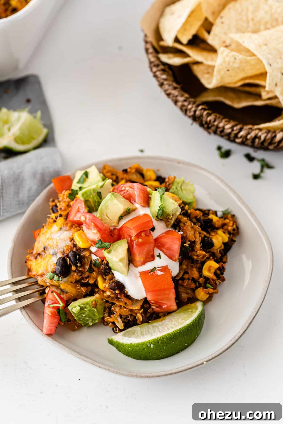 quinoa enchilada casserole on a white plate topped with sour cream, tomato, avocado, and lime