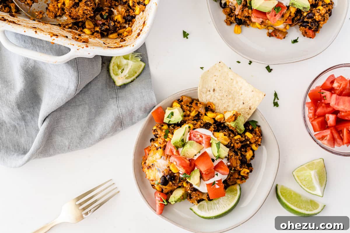 quinoa enchilada casserole on a white plate topped with sour cream, tomato, avocado, and lime