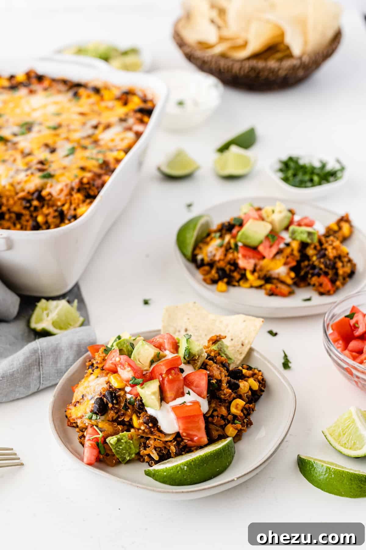 quinoa enchilada casserole on a white plate topped with sour cream, tomato, avocado, and lime