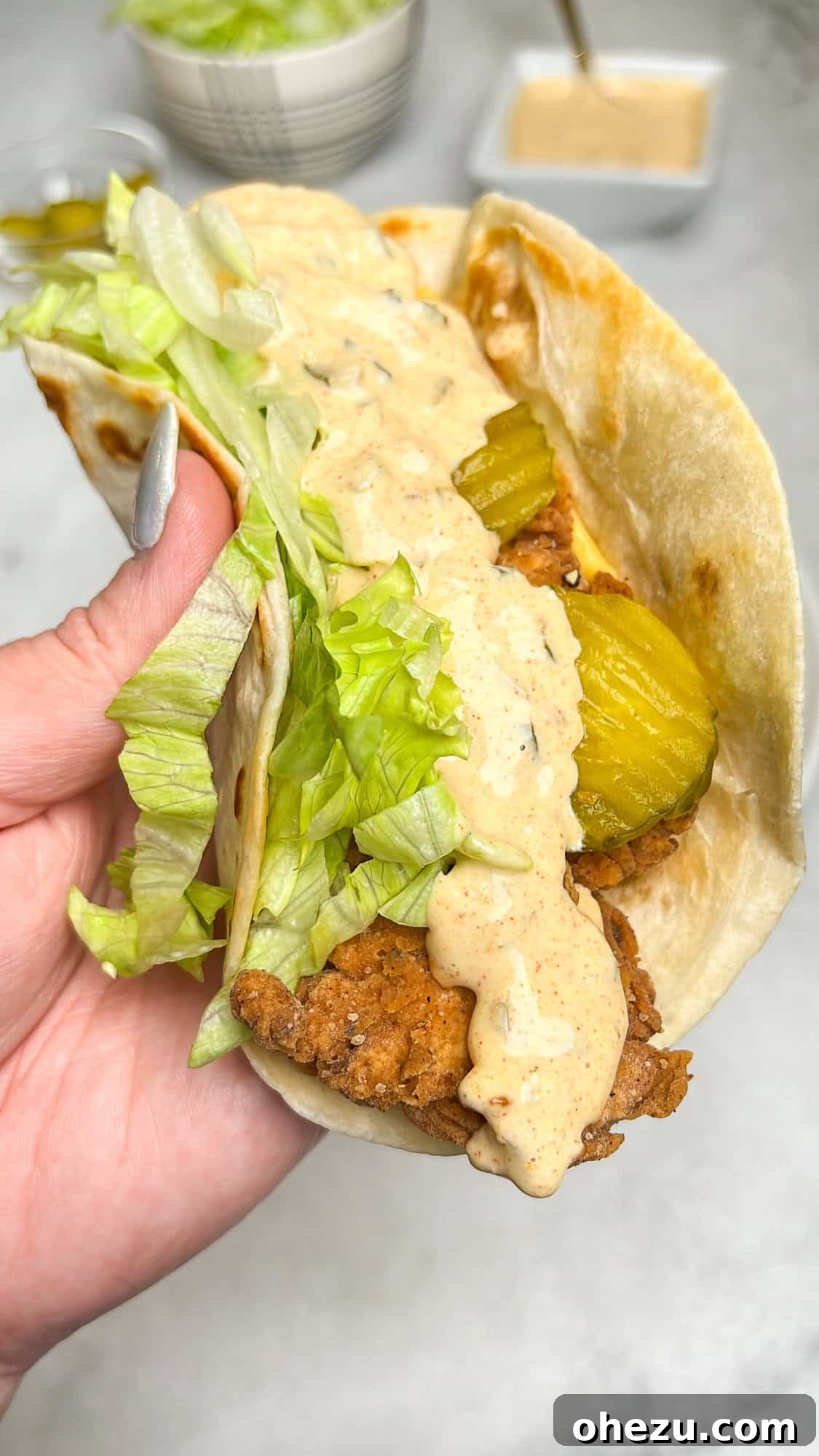 Ultimate Chicken Big Mac Taco 13 A hand holding a freshly assembled chicken Big Mac taco, highlighting the crispy chicken, sauce, lettuce, and pickles.