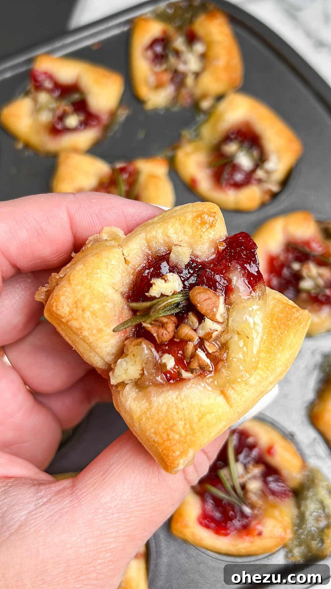 Flaky Cranberry Brie Bake 11 A hand reaching for a baked brie cranberry puff pastry bite, highlighting its deliciousness and ease of serving as a party snack.
