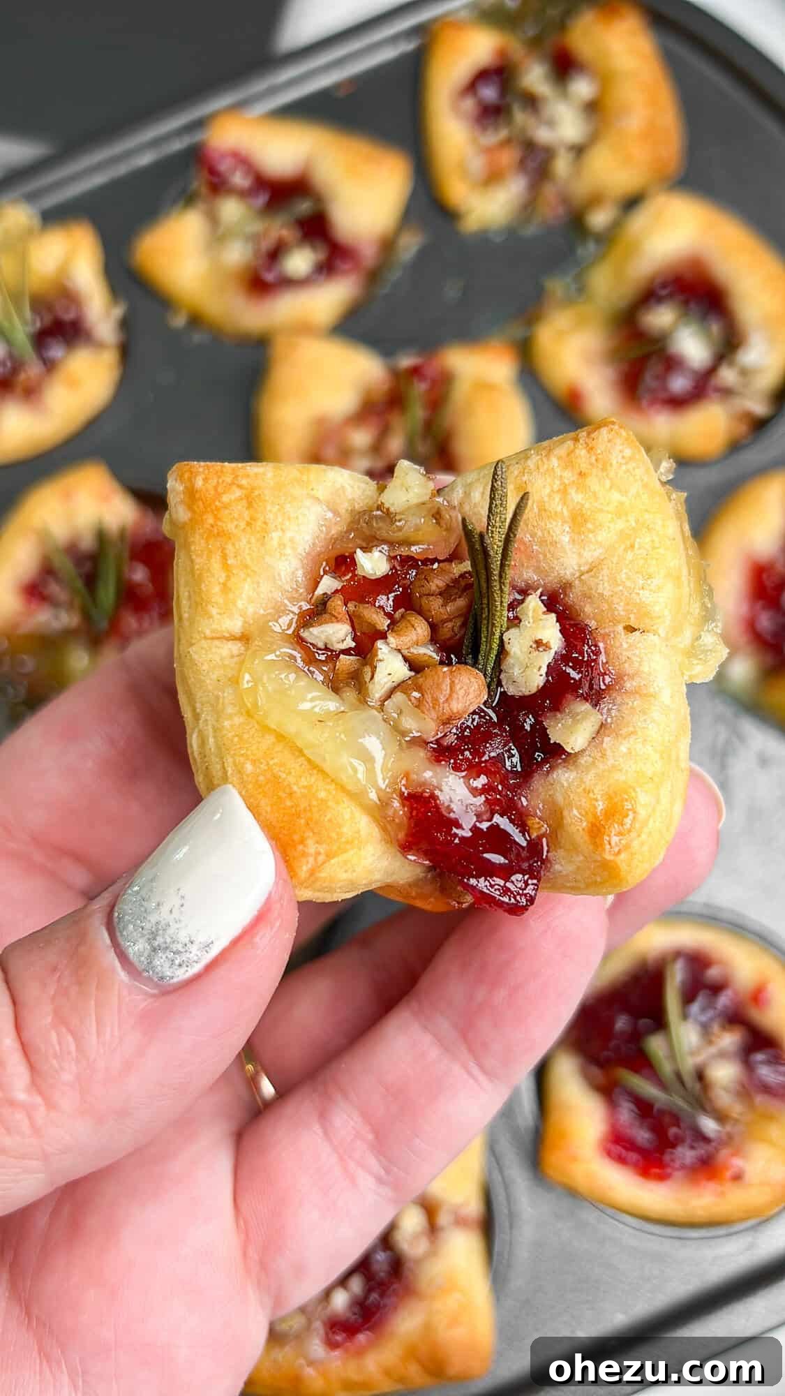 Flaky Cranberry Brie Bake 3 A hand gently holding a single baked brie and cranberry puff pastry bite, showcasing its golden crust and delicious filling, perfect for a handheld party snack.
