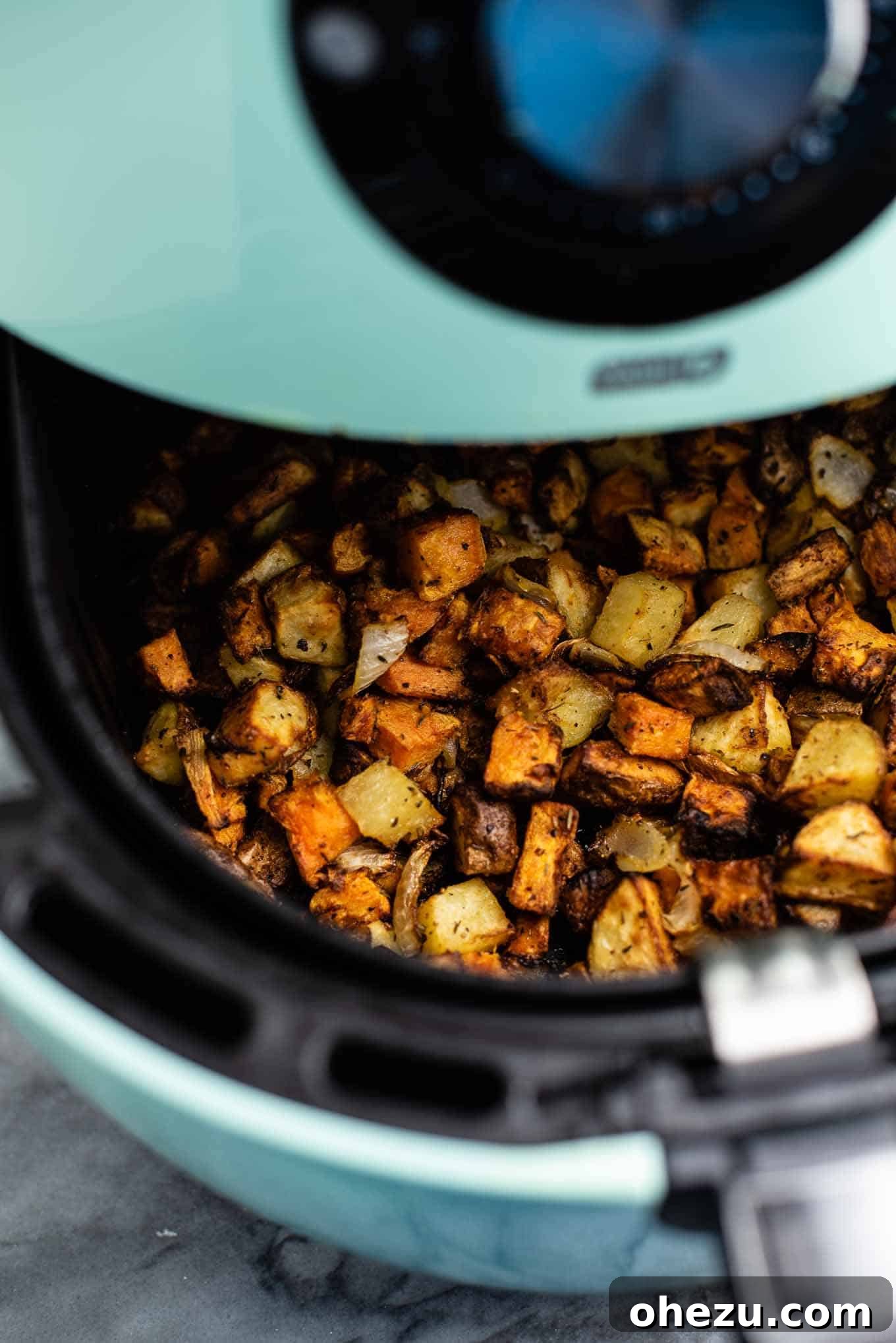 Air fried breakfast hash being pulled out of the air fryer basket, steam rising.