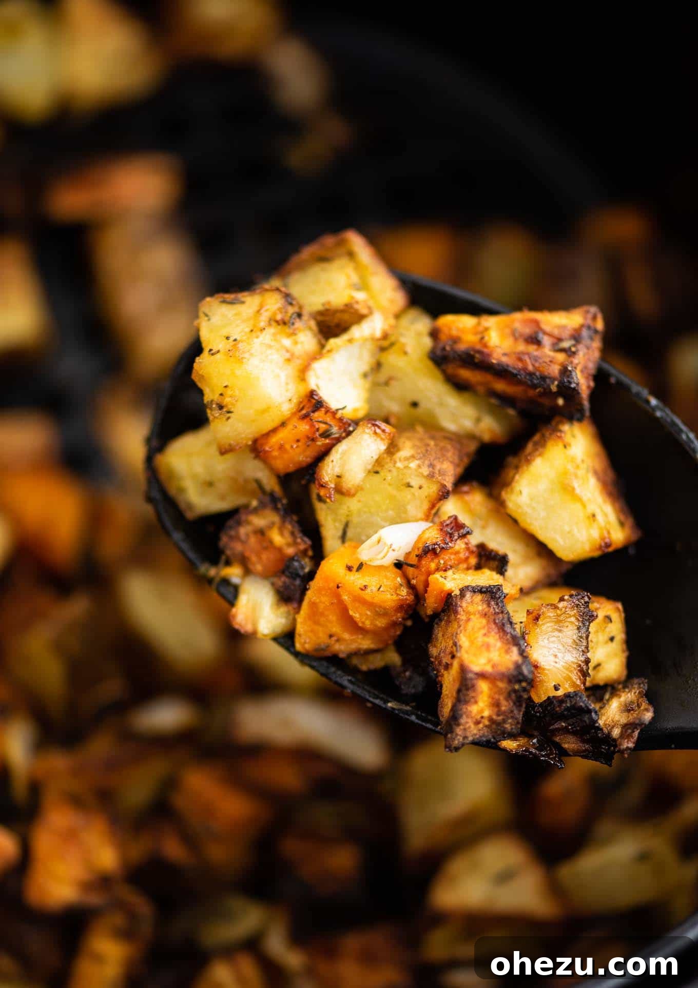 Close-up of sweet potatoes, russet potatoes, and onions on a black serving spoon.