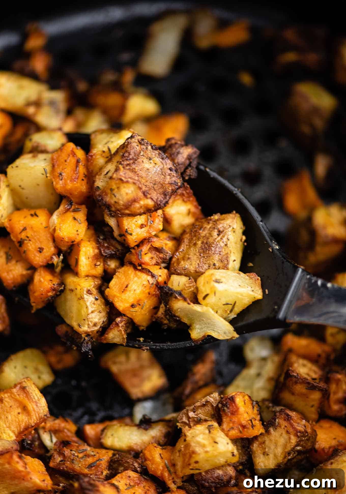 Air fried sweet and russet potatoes on a serving spoon, highlighting their mixed texture.