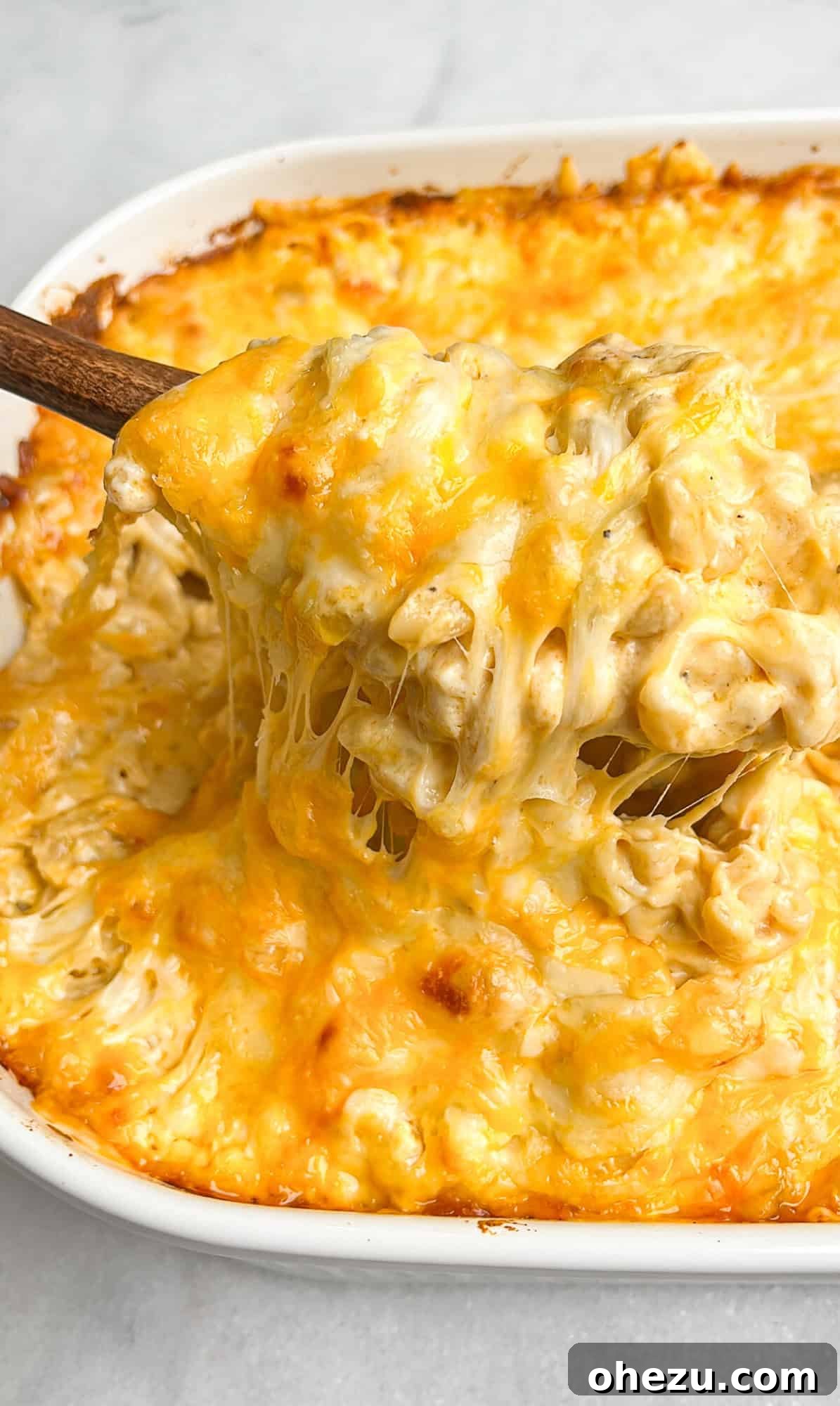 Gooey macaroni and cheese being lifted out of pan with a spoon, showcasing its rich, melted texture.