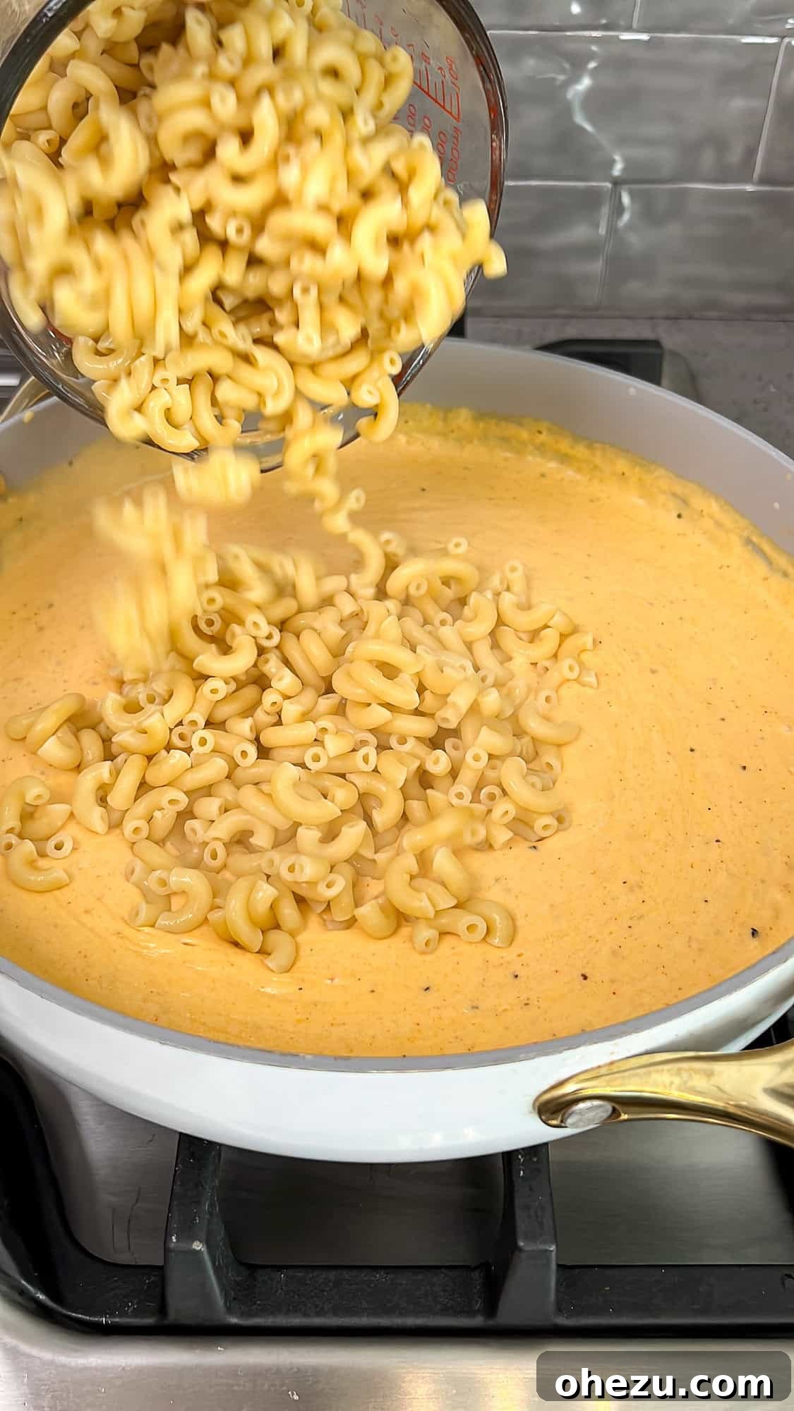 Cooked macaroni being added to the rich, creamy cheese sauce in a pan.