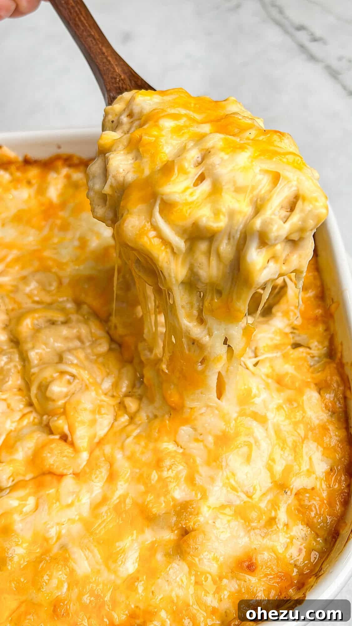 A large serving of gooey cheese macaroni and cheese being lifted out of a pan with a spoon, highlighting the stretch and melt.