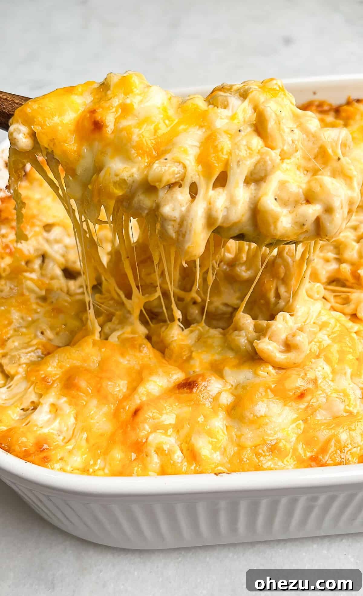 A spoonful of gooey macaroni and cheese being lifted from the pan, showcasing its rich, stringy texture.