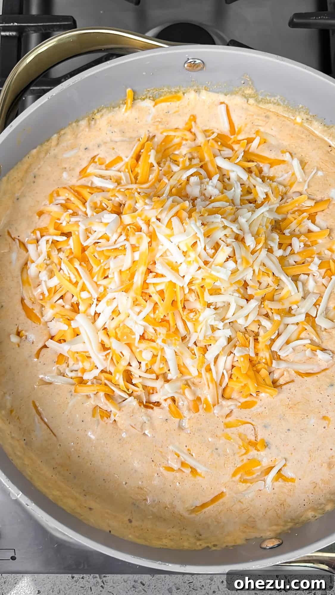 Shredded cheese gradually melting into the simmering cream sauce, creating a smooth blend.