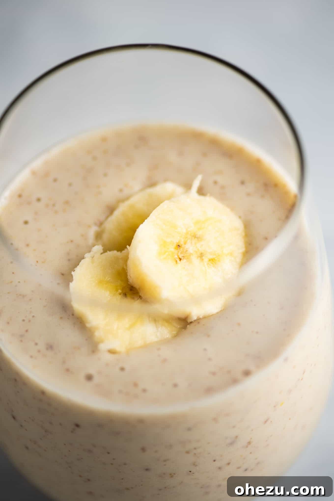 Banana Bliss 4 A close-up shot of the creamy banana smoothie in a clear glass, with a single banana slice delicately placed on the rim for garnish, highlighting its appealing texture.