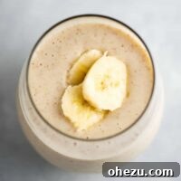 A close-up of a creamy banana smoothie in a glass, beautifully garnished with fresh banana slices on top.