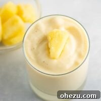 A frosty pineapple smoothie in a glass with frozen pineapple on top, showcasing the perfect thick texture.