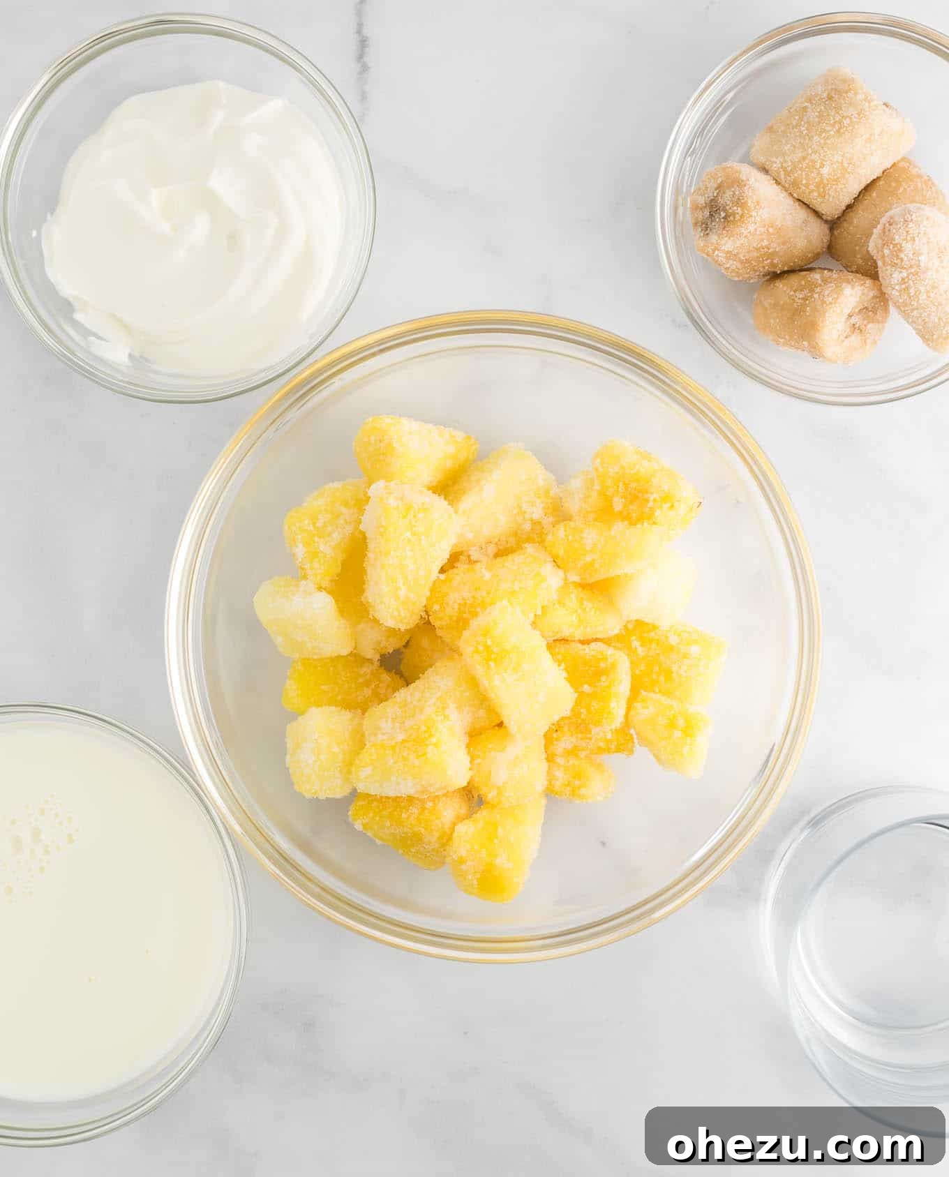 Golden Pineapple Chill 6 Individual clear bowls containing the four main ingredients: frozen pineapple chunks, creamy Greek yogurt, frozen banana chunks, and a glass of almond milk, neatly arranged for the camera.