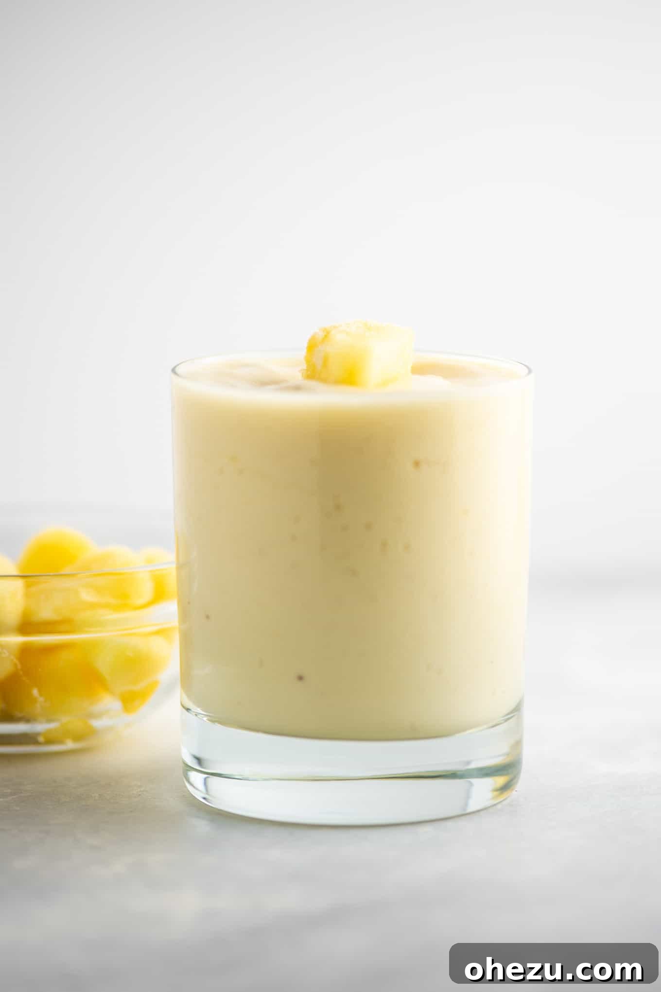 Golden Pineapple Chill 9 A pineapple smoothie in a glass cup, with fresh pineapple slices and green leaves in the background, suggesting a tropical setting.