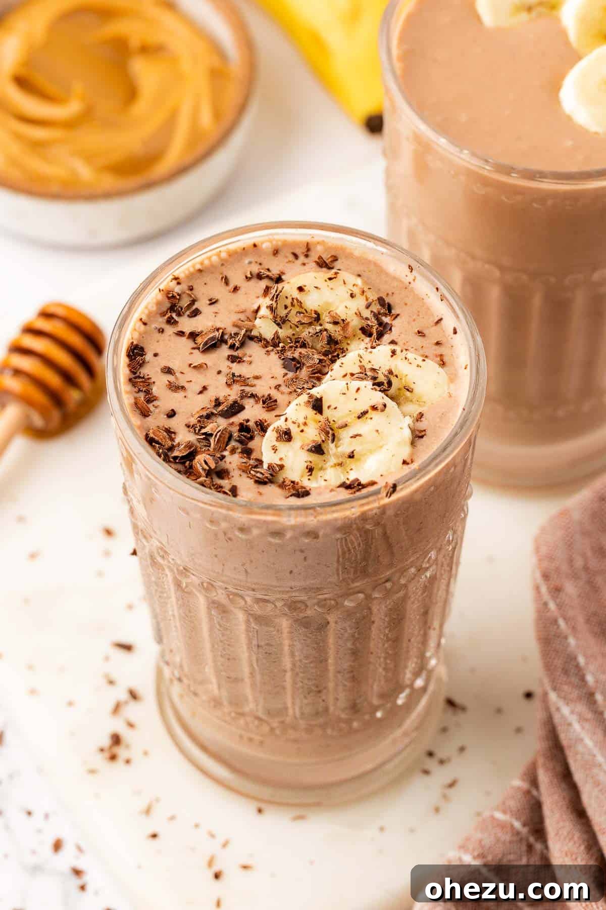 A chocolate peanut butter banana smoothie topped with chocolate shavings and fresh banana slices, served in a glass.