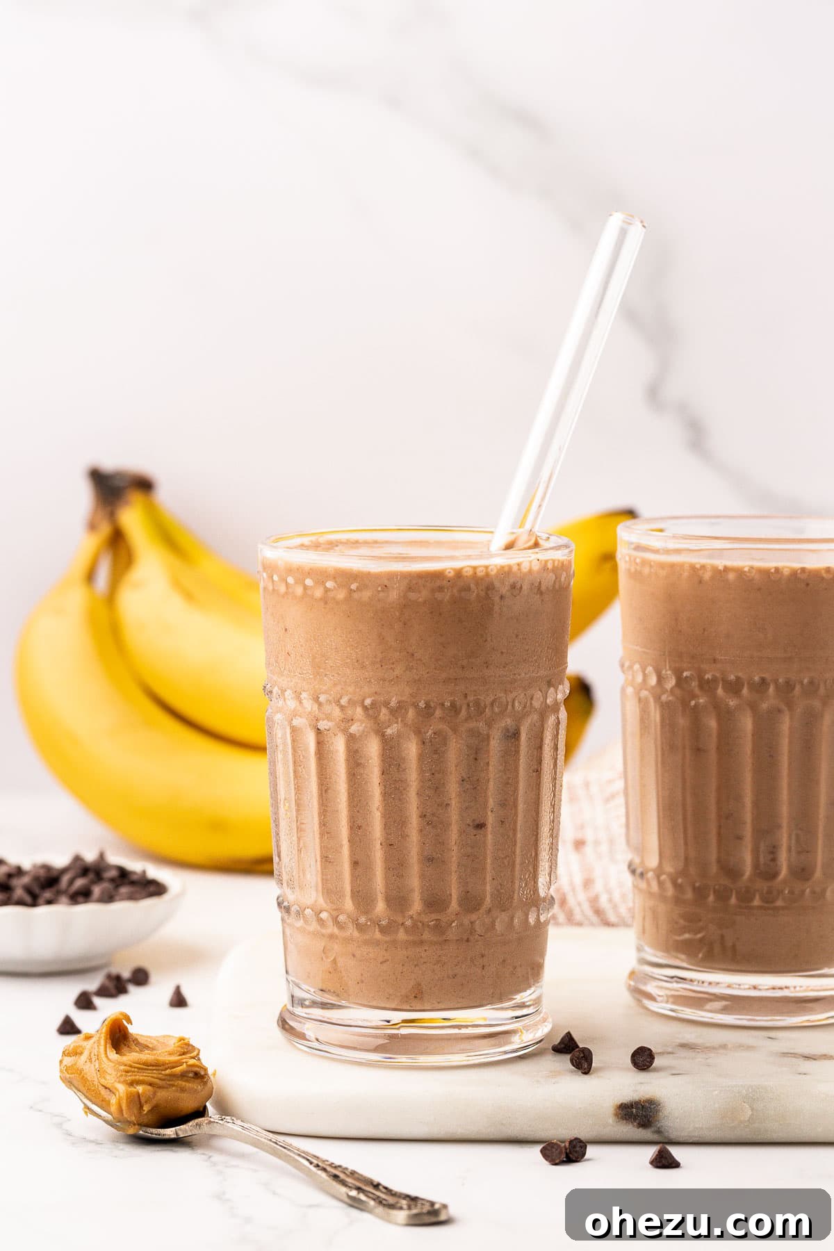 A chocolate peanut butter banana smoothie in a clear glass with a straw, ready to drink.