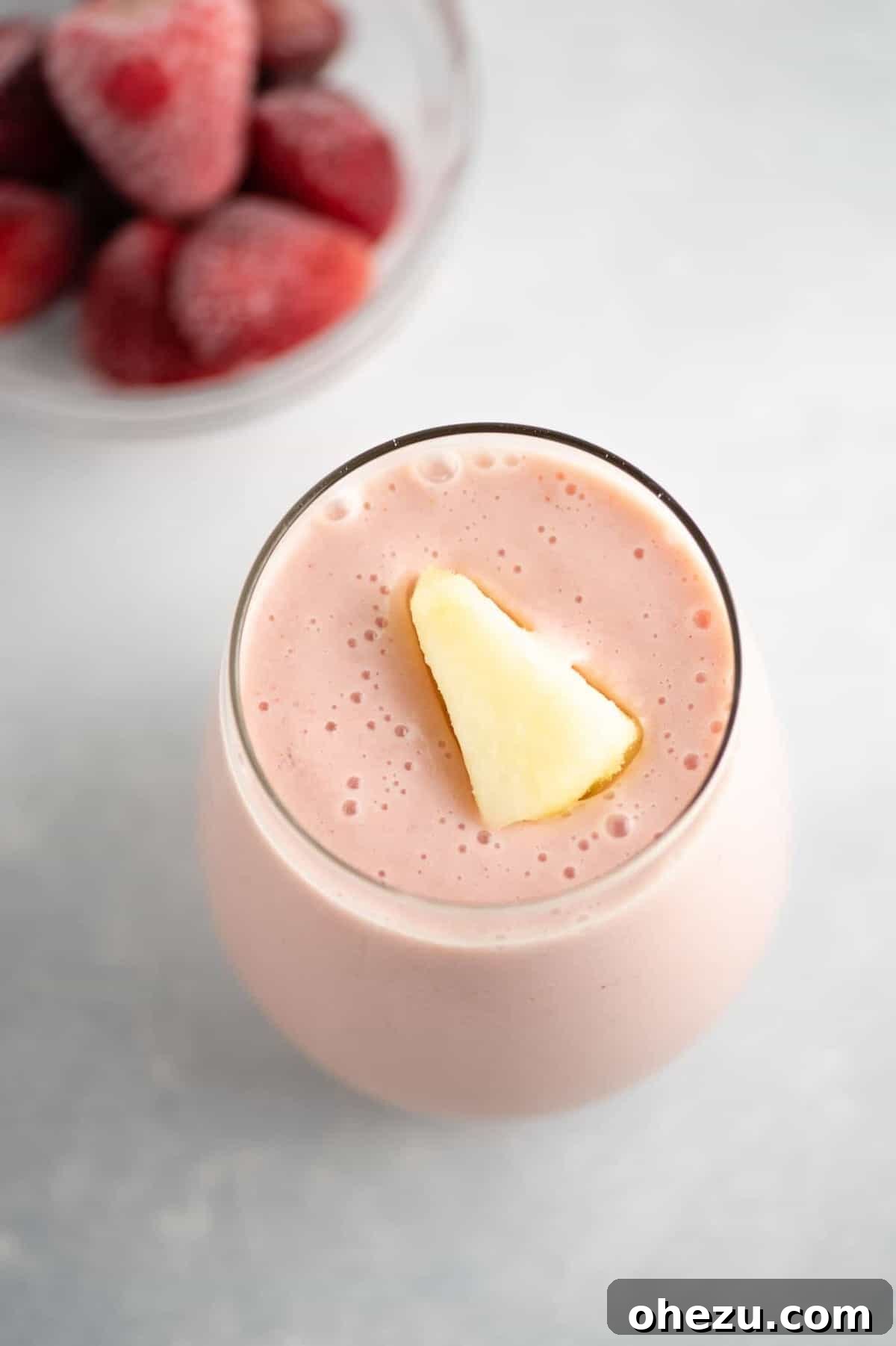 Strawberry Pineapple Paradise 2 Vibrant pink strawberry pineapple smoothie in a glass with a frozen pineapple piece on top, ready to enjoy
