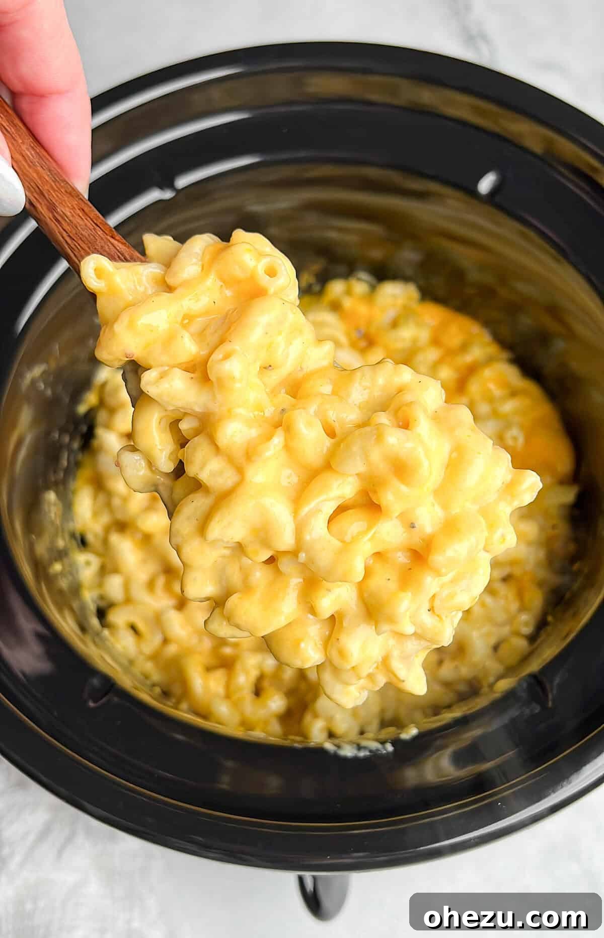 A serving spoon scooping creamy mac and cheese out of a slow cooker, showcasing its rich, golden texture.